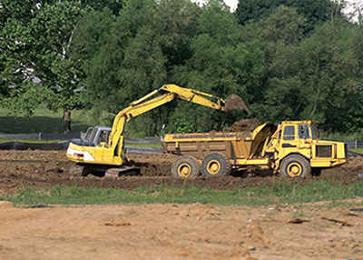 Backhoe unloading dirt from dump truck